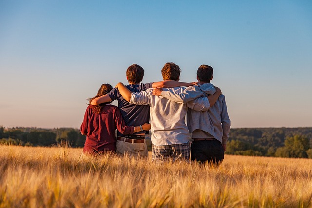 Four friends standing side-by-side with arms around each other's shoulders in a field, captured in a cool, editorial magazine style representing human connection and solidarity.